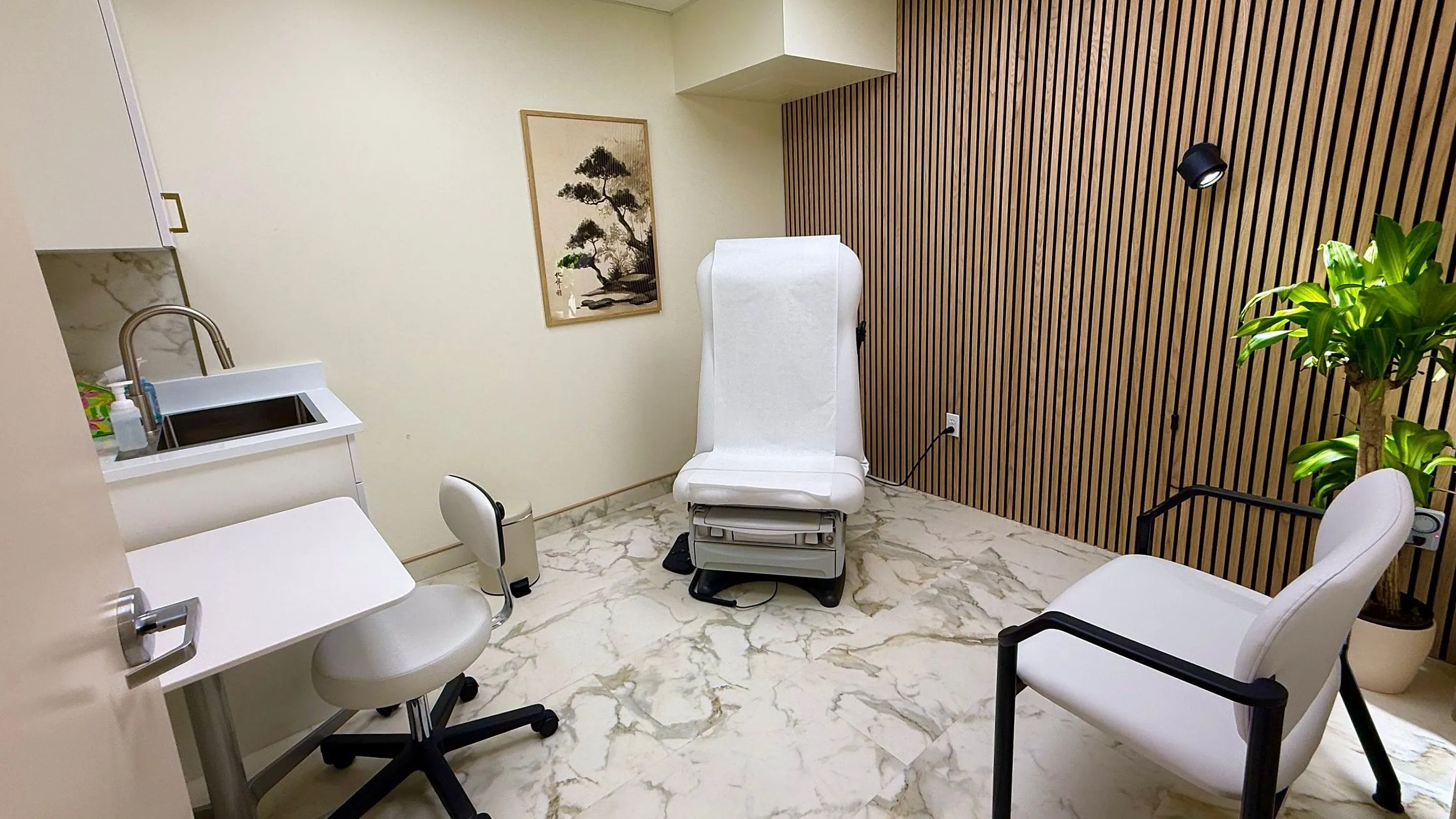 An examination room at the clinic: a slatted wood wall, an examination chair, a sink counter, and a chair for whoever came along